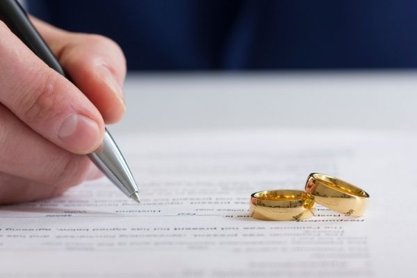 Man signing wedding documents with rings on paper